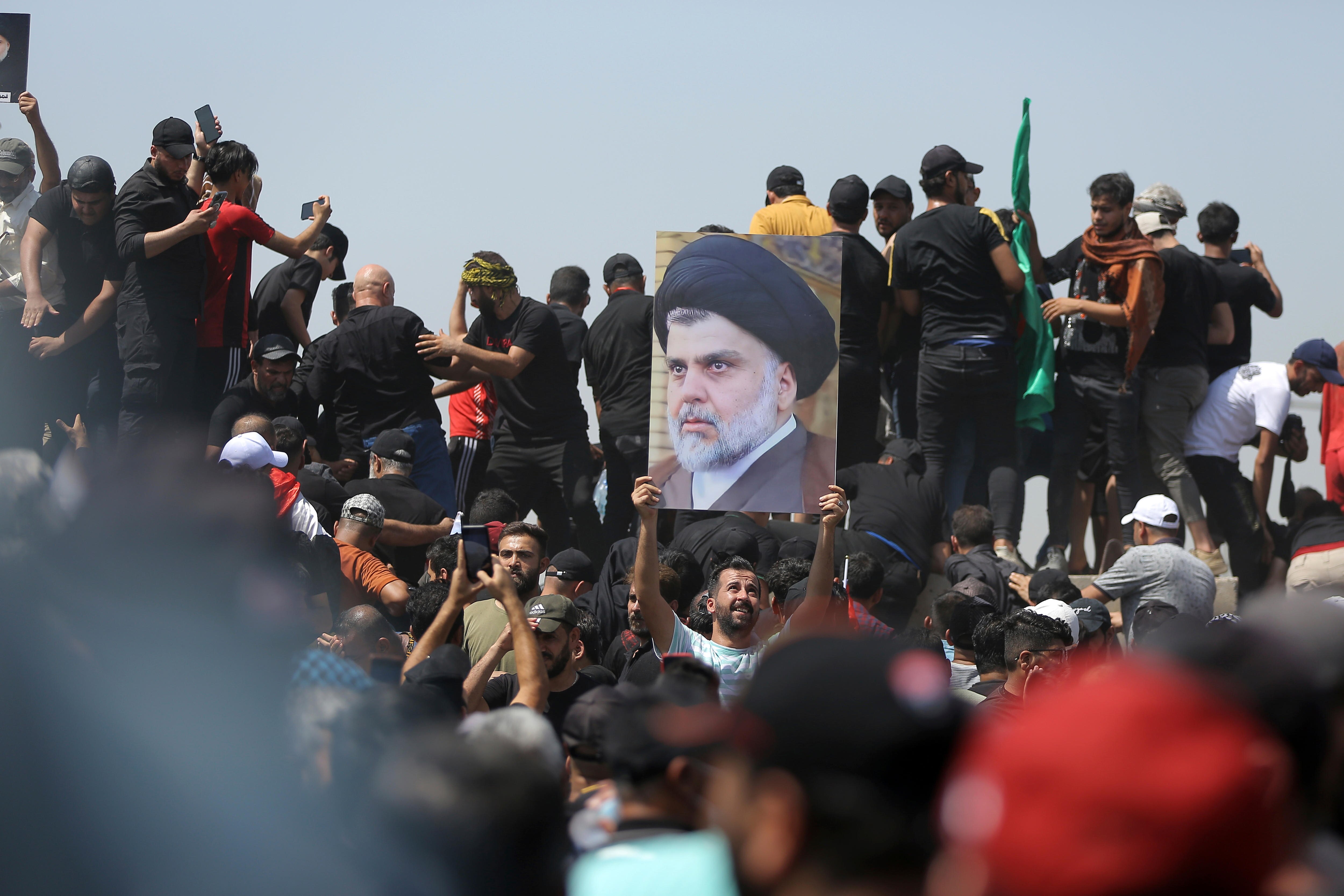 Man in a large crowd holds up poster with a photograph of Shiite cleric Muqtada al-Sadr.