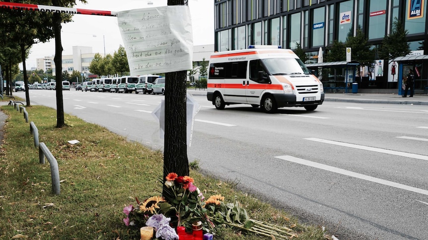 A note is left on a pole and flowers are left underneath on the side of a road