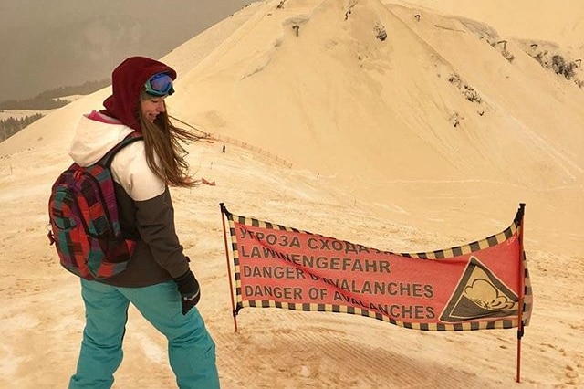 A snowboarder riding down an orange ski slope in front of a danger sign.