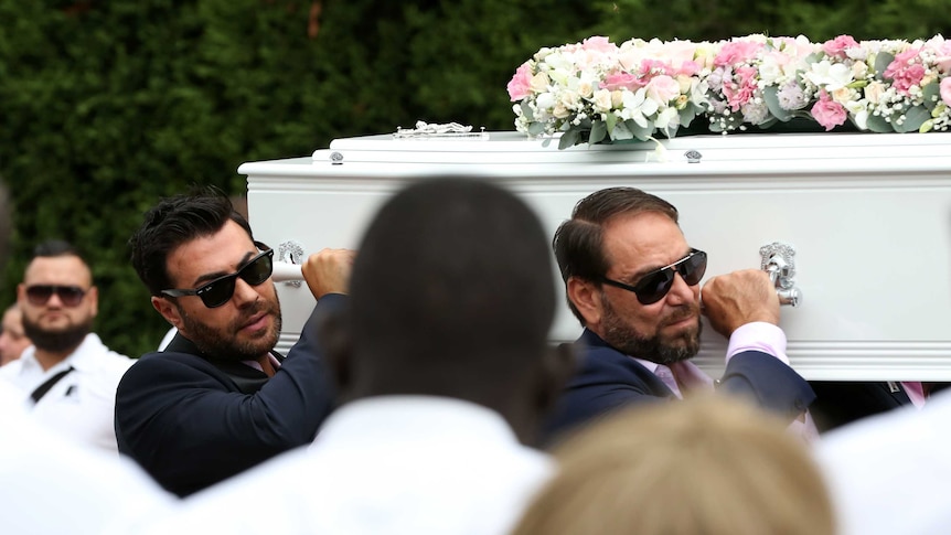 Two men in sunglasses carry a white coffin