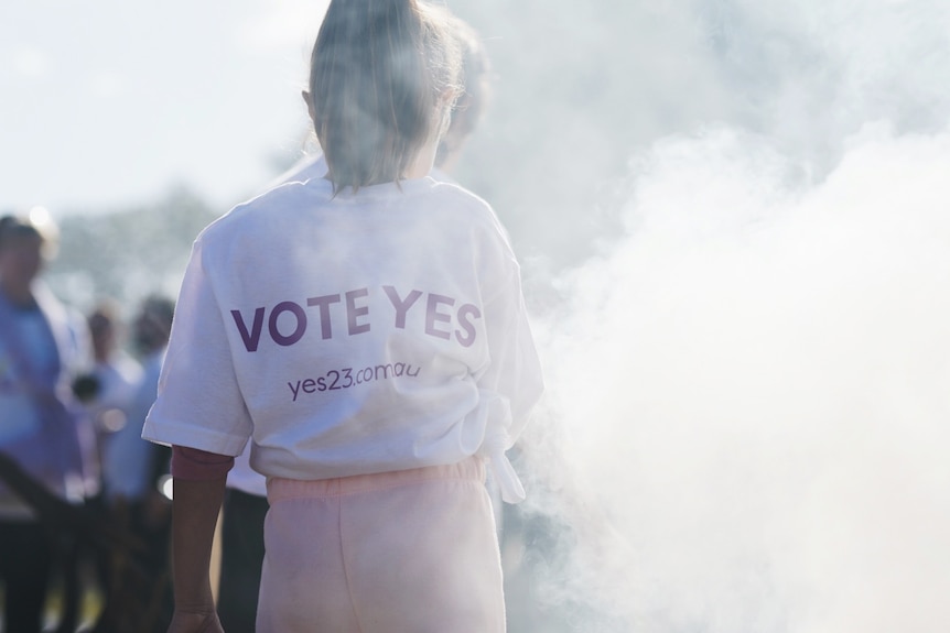 A person wearing a 'vote yes' shirt walks through a cloud of smoke at the Come Together For Yes rally in Sydney