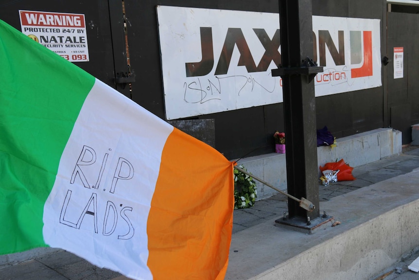 An Irish flag and several bunches of flowers lie outside the entrance to Jaxon construction's East Perth site.