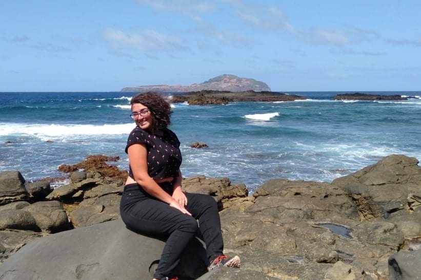 A woman sits on a rock at the edge of a shoreline