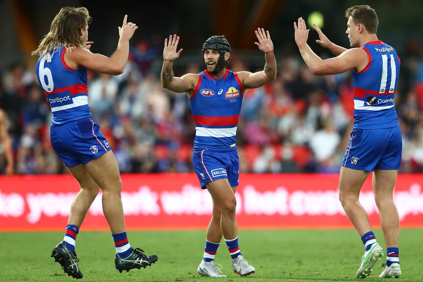 Three AFL players give each other a high-five during a match 