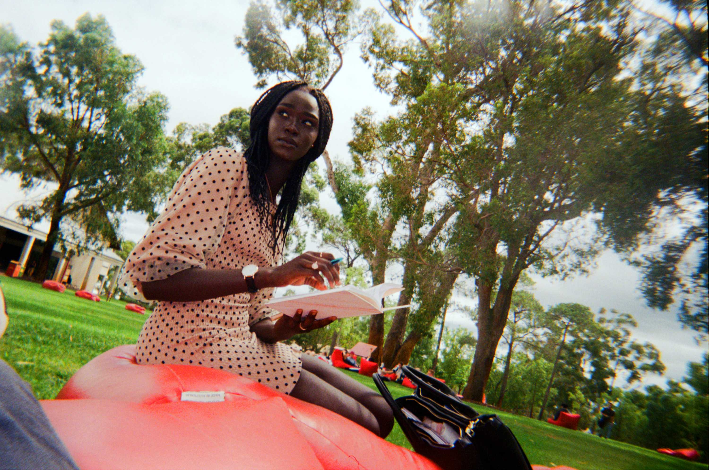 A young African-Australian woman sits on a red bean bag in the middle of a park