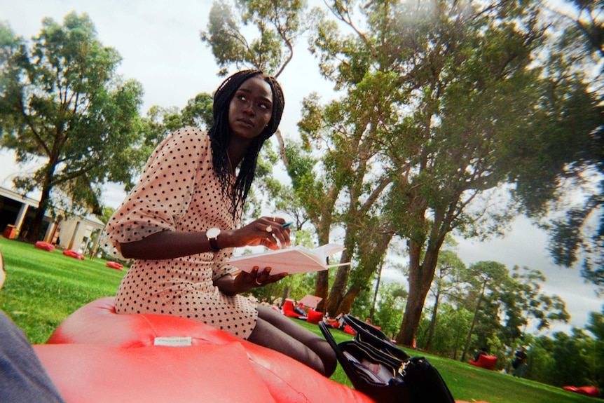 A young African-Australian woman sits on a red bean bag in the middle of a park