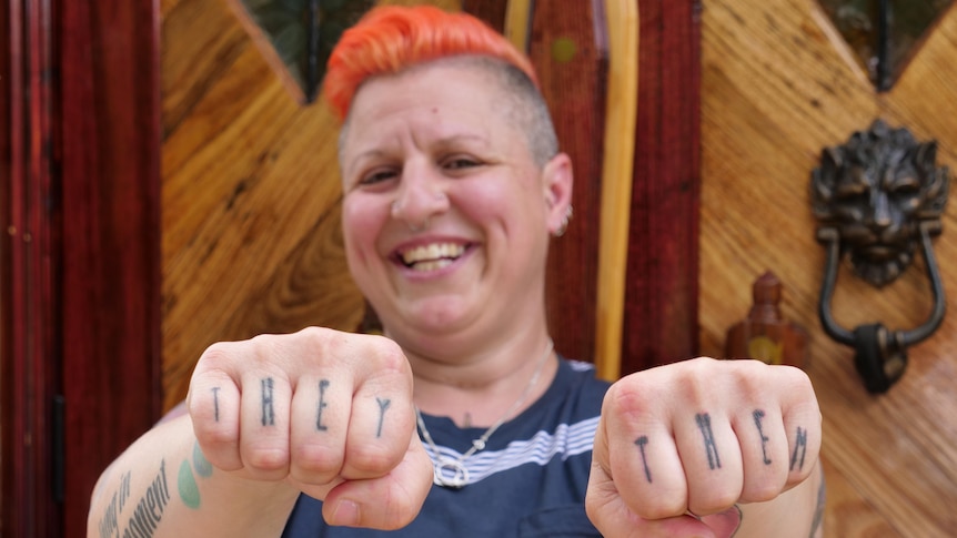 A person holding up their knuckles that say they/them in tattoos. 