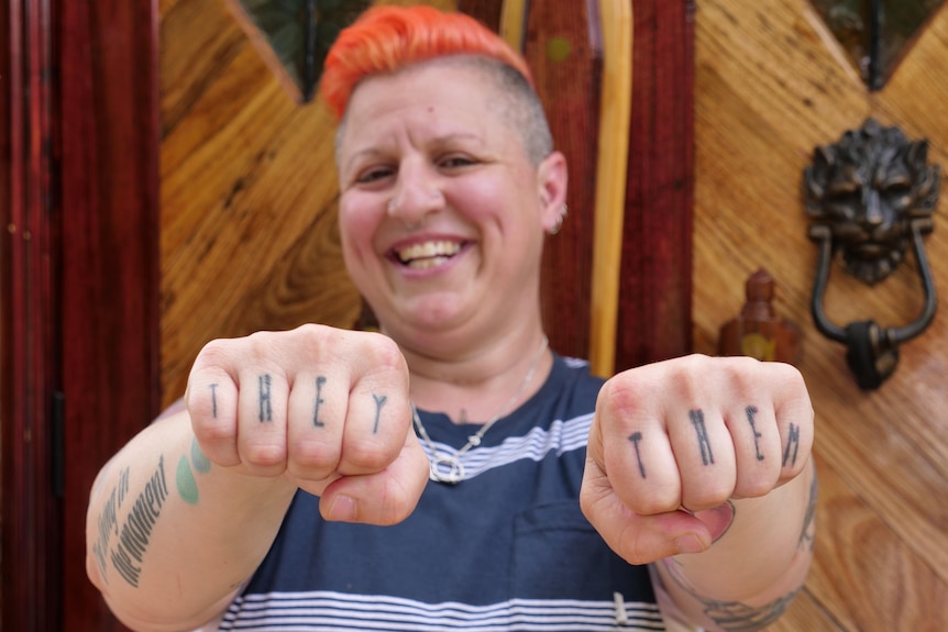 A person holding up their knuckles that say they/them in tattoos. 