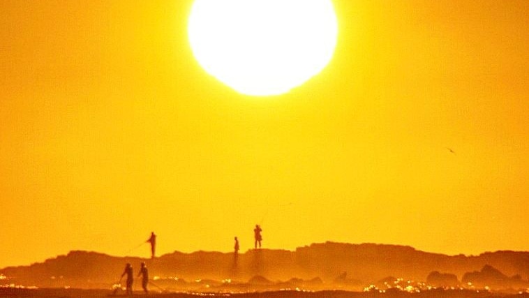 A sunrise over the ocean with people fishing in the foreground