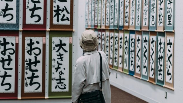 A person in a hat looks at calligraphy on a wall.