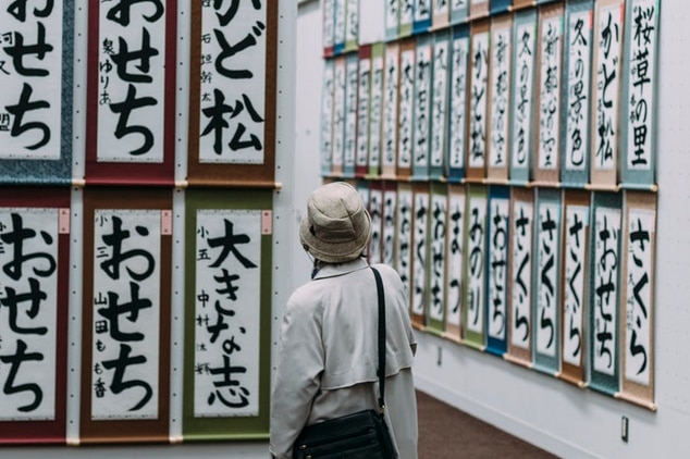 A person in a hat looks at calligraphy on a wall.