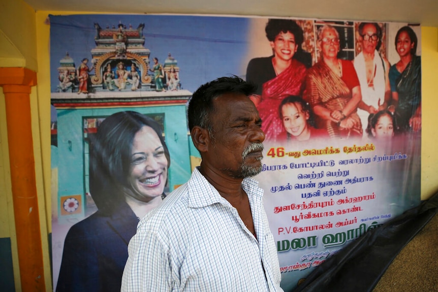 An Indian villager stands in front of a banner displaying photographs of U.S. Vice President-elect Kamala Harris.