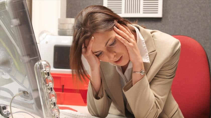 Woman looking stress with her head in her hands sitting at her desk.