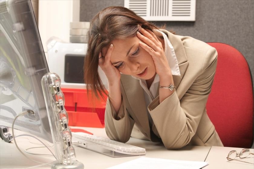Woman looking stressed with her head in her hands sitting at her desk.