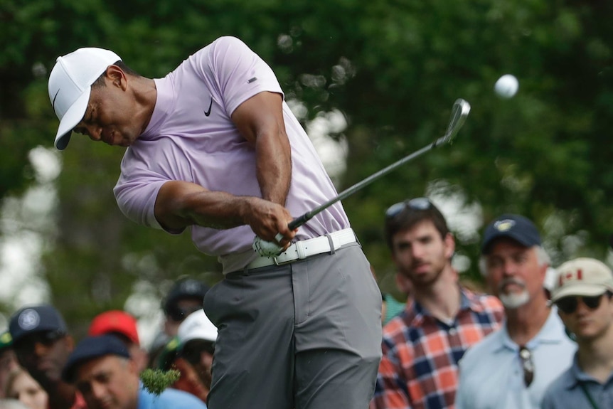 Tiger Woods closes his eyes as he hits a shot, with spectators watching on in the background