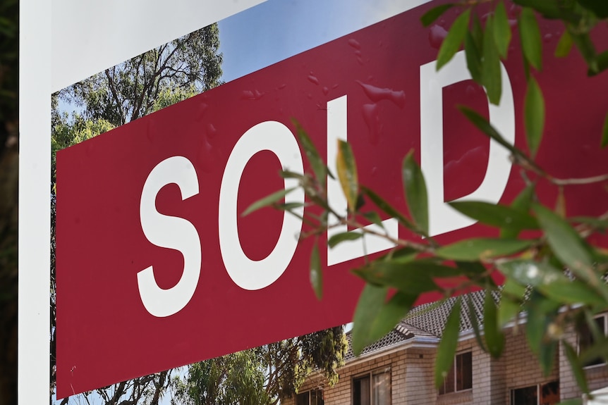 A sticker that reads 'SOLD' on a real estate sign outside a property.