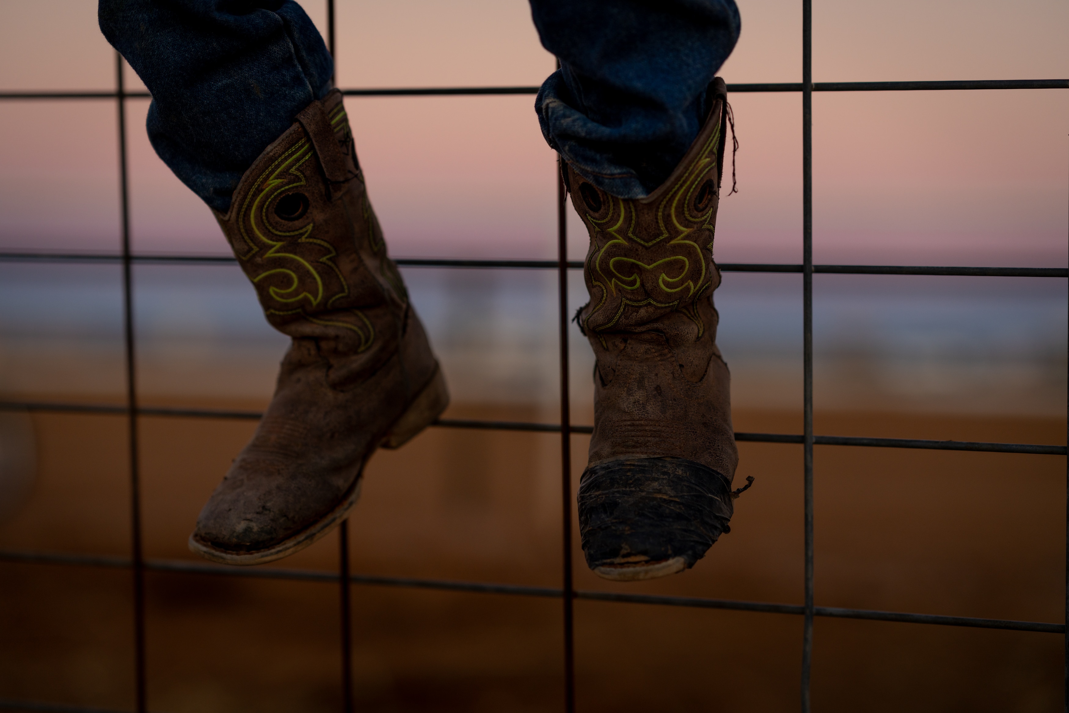 A child's feet wearing brown cowboy boots with bright green stitching design