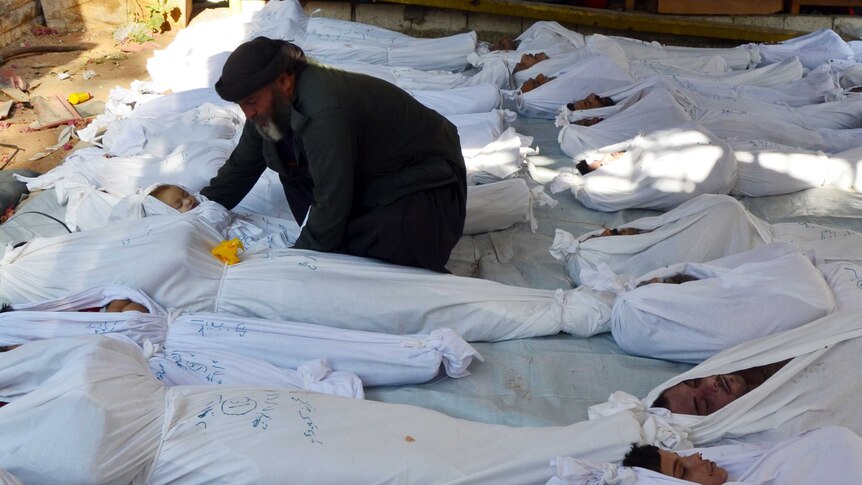 A man holds the body of a dead child among bodies of people wrapped in white sheets