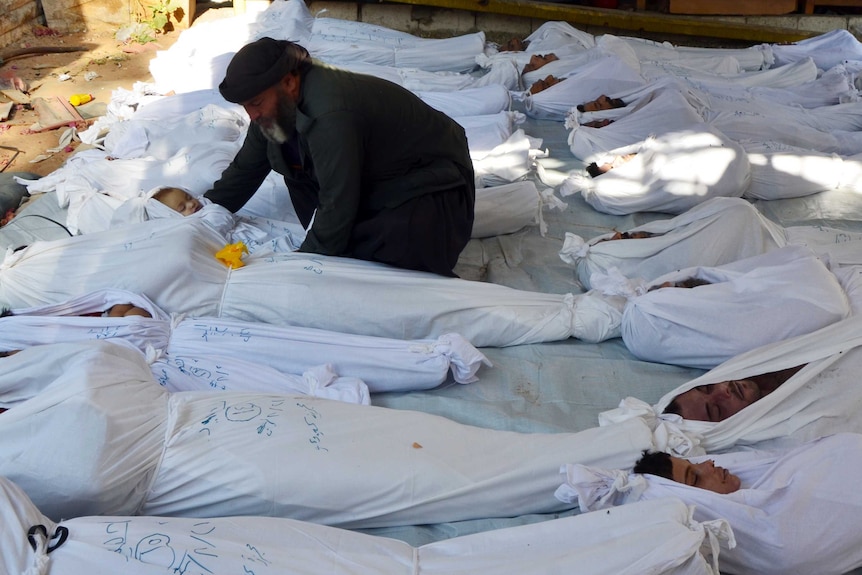 A man holds the body of a dead child among bodies of people wrapped in white sheets