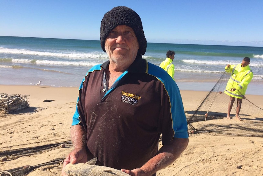 Commercial fisherman on Port Macquarie beach holding a mullet