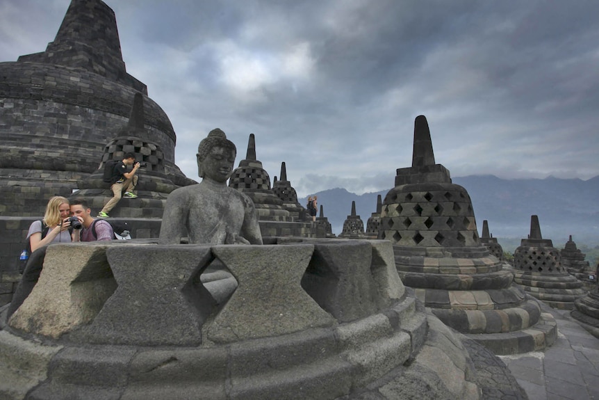 Tourists take photos amongst statues of the ancient temple.