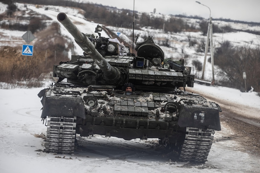 A tank drives along a road outside a snowy frontline town.