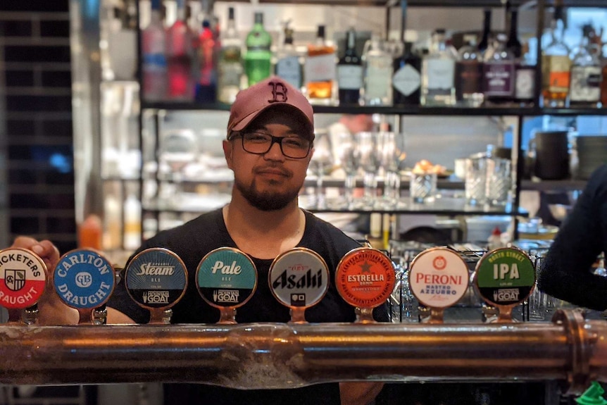 A man wearing a cap stands behind a bar.