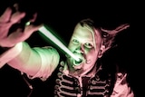 A circus performer holds a neon sword and slides it into his mouth.