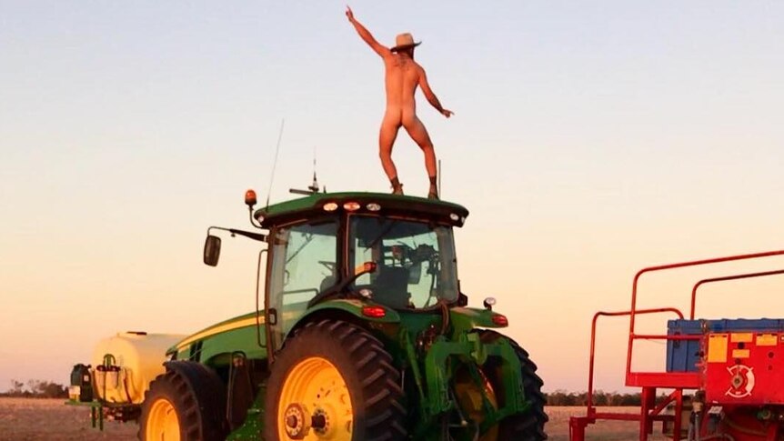 A farmer from Dirranbandi, Queensland stands naked on a tractor at sunset