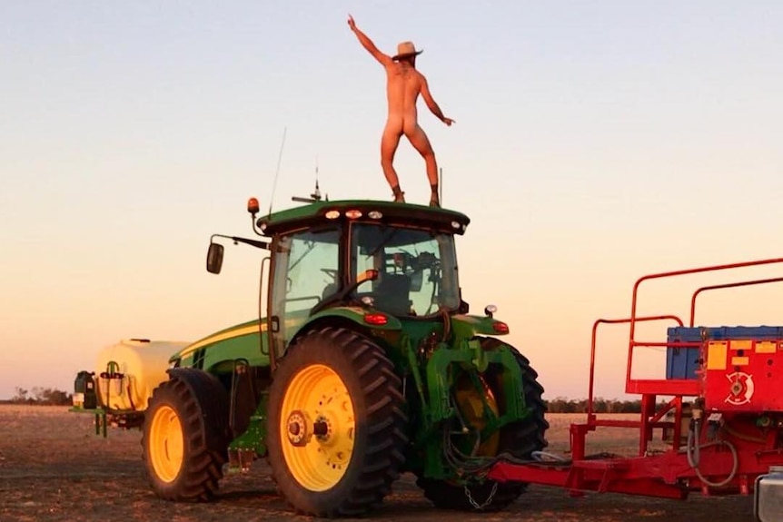 A farmer from Dirranbandi, Queensland stands naked on a tractor at sunset