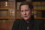 Victorian Chief Magistrate Lisa Hannan sits in front of a shelf of books giving an interview.