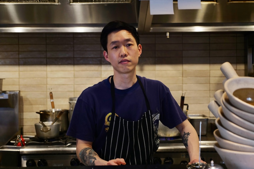 A man in a chef apron smiles while standing in a restaurant kitchen