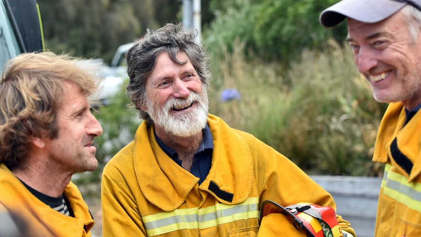 Three men in yellow firefighting uniforms chat and laugh together