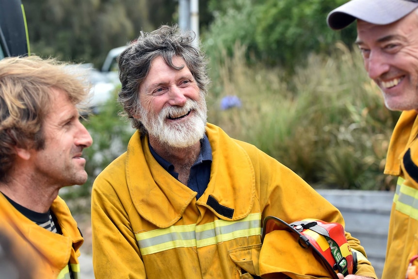 Three men in yellow firefighting uniforms chat and laugh together