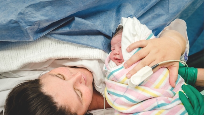 A woman in a hospital bed holding a newborn baby.