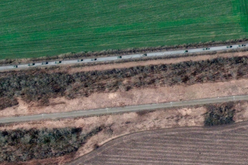 A satellite image shows an overview of a convoy of armored vehicles and trucks moving past fields.