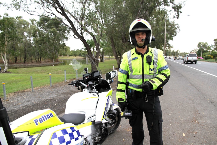 A police officer wearing a high viz jacket, stands beside his motorcycle