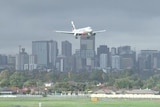 A silver aeroplane lands over a city