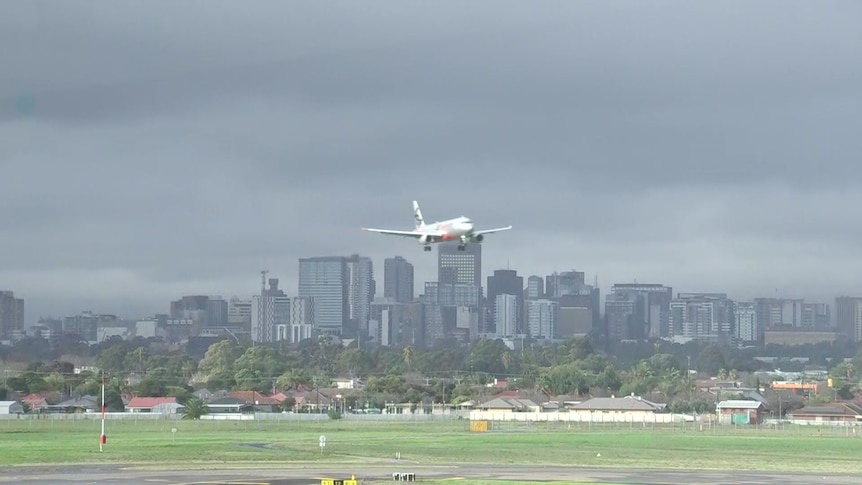 A silver aeroplane lands over a city