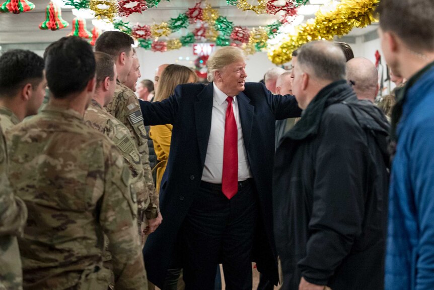 US President Donald Trump puts his arms around soldiers in a dining hall that has tinsel strung from the ceiling