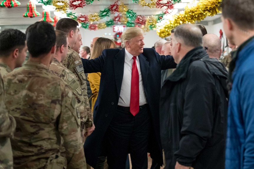 US President Donald Trump puts his arms around soldiers in a dining hall that has tinsel strung from the ceiling