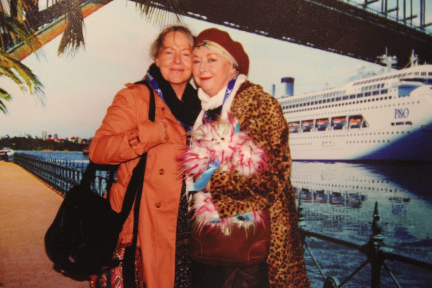 Karen Borger (r) with her Winner bear and her sister stand on the edge of Sydney harbour with a cruise ship behind them.