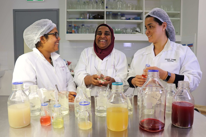 Yasmina Sultanbawa (centre) and two colleagues smile standing in a lab wearing white coats.