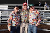 Three men stand tofether at a cattle saleyard