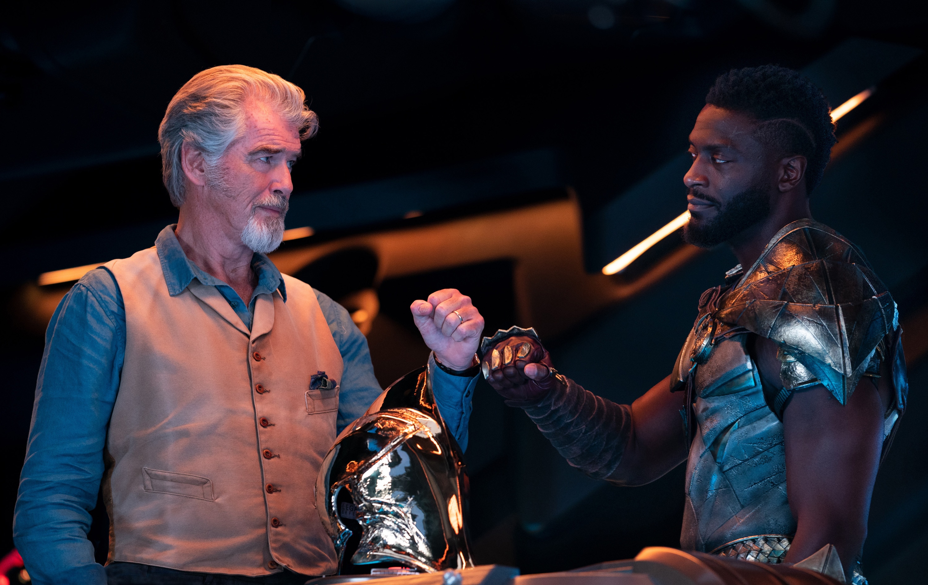 A well-dressed older man and a Black man in armour look at each other. They each have their hands in fists.