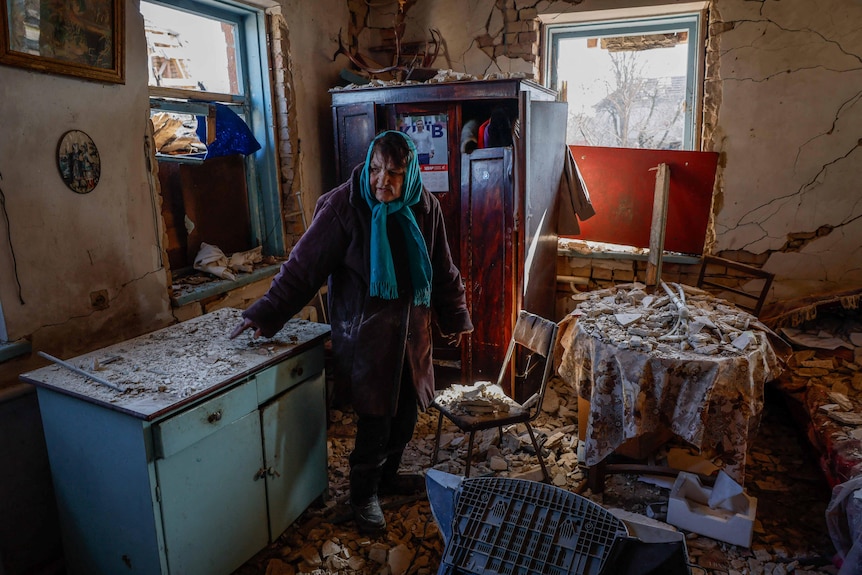 Woman in a head scarf stands in destroyed home 