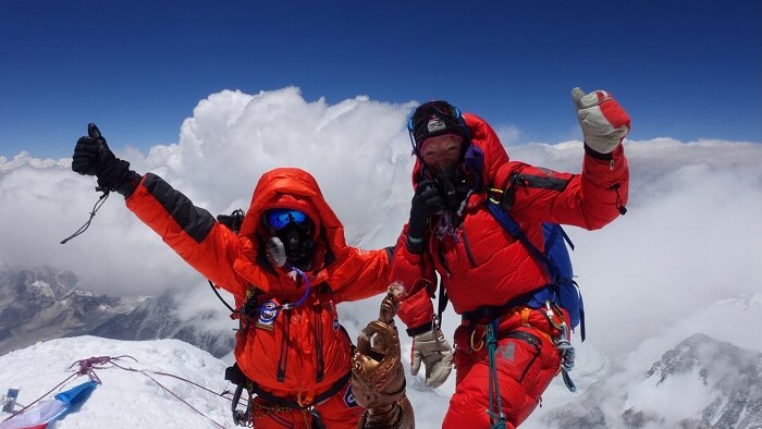 Two female mountain climbers in red outfits raise their arms on the summit of Mount Everest