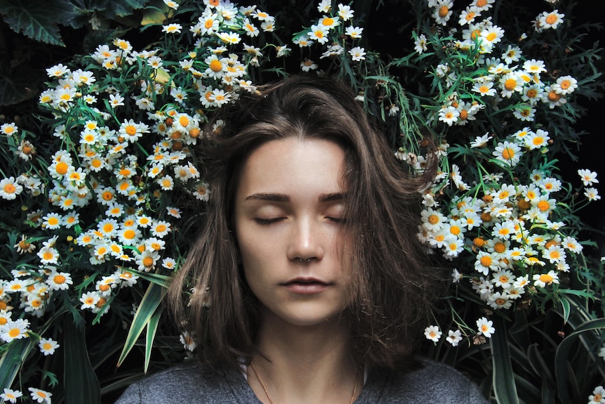 A woman's face, her eyes closed and head surrounded with flowers.