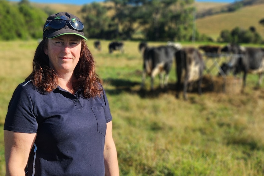 Farmer Wendy Whelan stands in a paddock, with cows, trees and hills in the background.