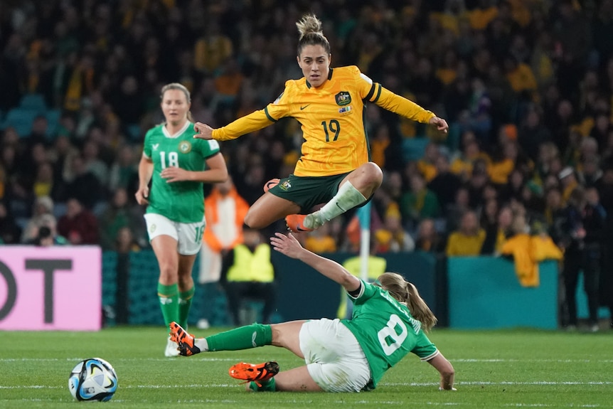 Matildas player Katrina Gorry jumps in air over an England player while playing a soccer match